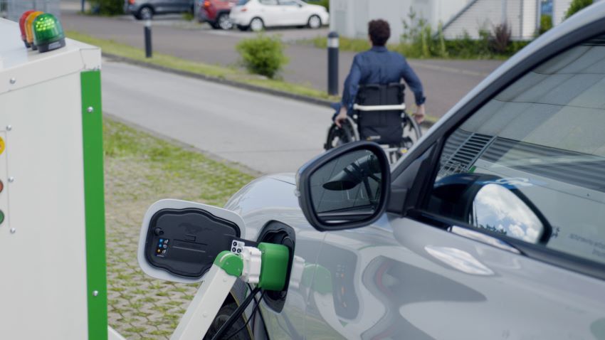 Robô carrega carro enquanto pessoa com deficiência se move por calçada