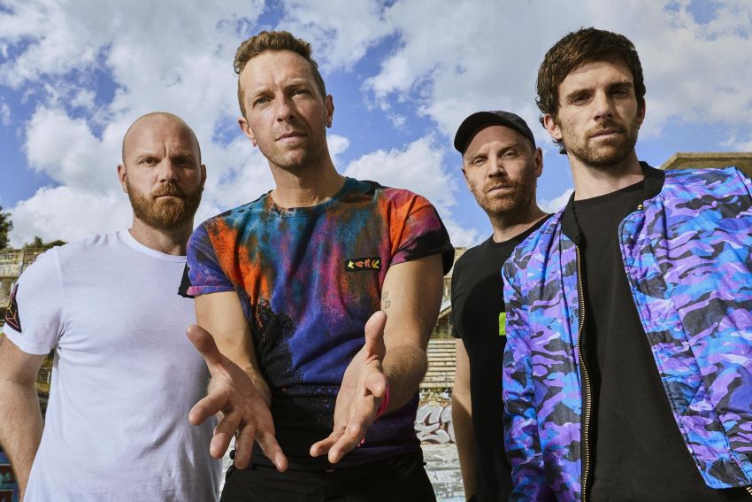Integrantes da banda Coldplay posam para foto com céu azul de fundo
