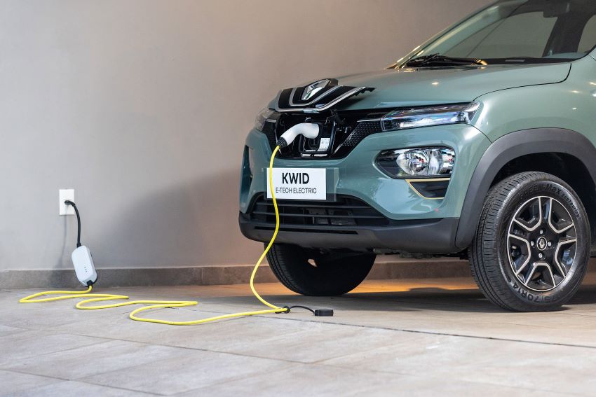 Imagem mostra em detalhe um Renault Kwid concetado à uma tomada comum na garagem de uma casa