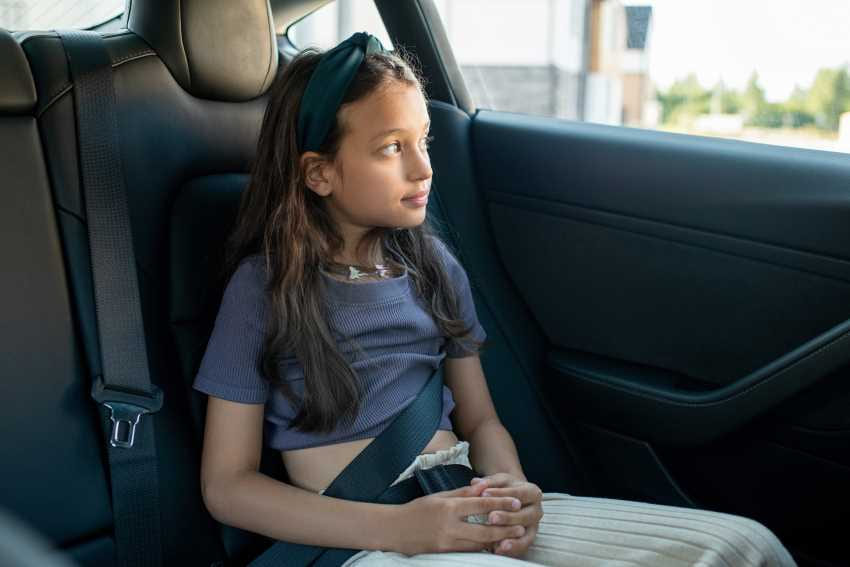 Garota olhando para a fora do carro usando cinto de segurança