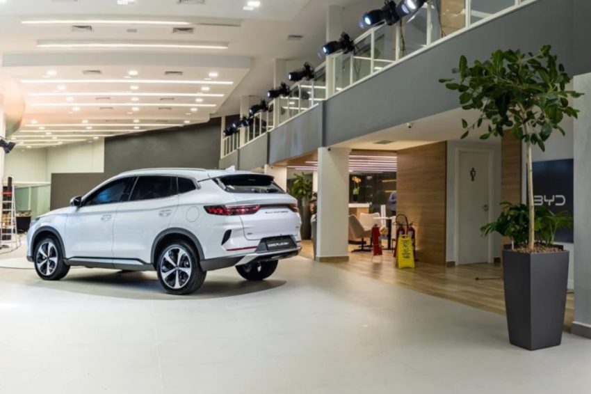 Carro branco da BYD está em exibição dentro de concessionária.