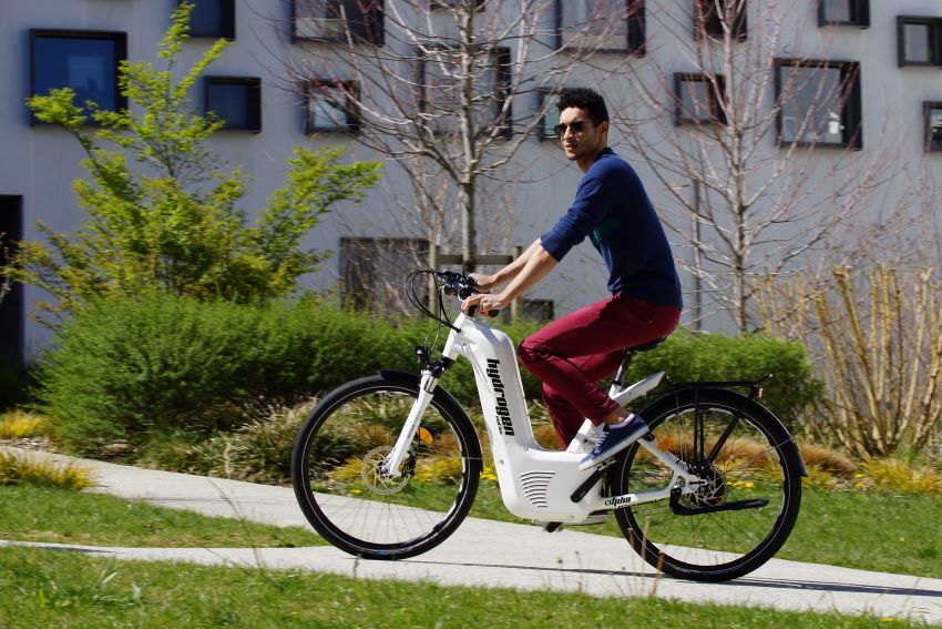 Homem de camiseta azul e calça vermelha em cima de uma bicicleta movida a hidrogenio