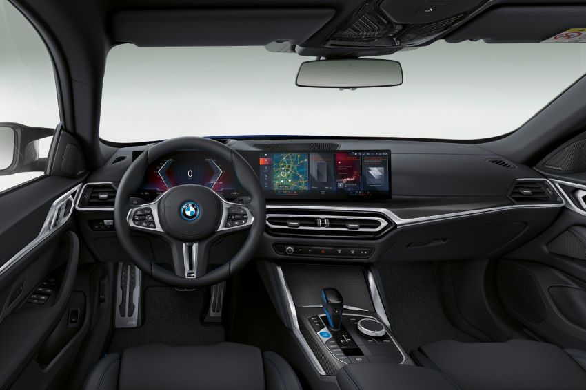 Foto do interior do bmw i4, ode se ve o volante, painel, parte dos bancos e cambio. Tudo na cor preta com detalhes em prata.