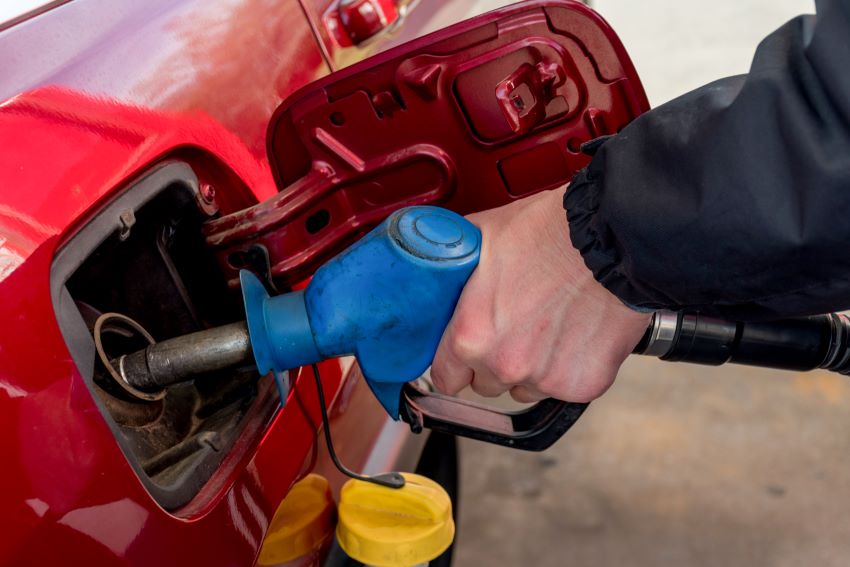 Imagem mostra em detalhe mão de uma pessoa colocando combustível por meio de mangueira em um carro vermelho