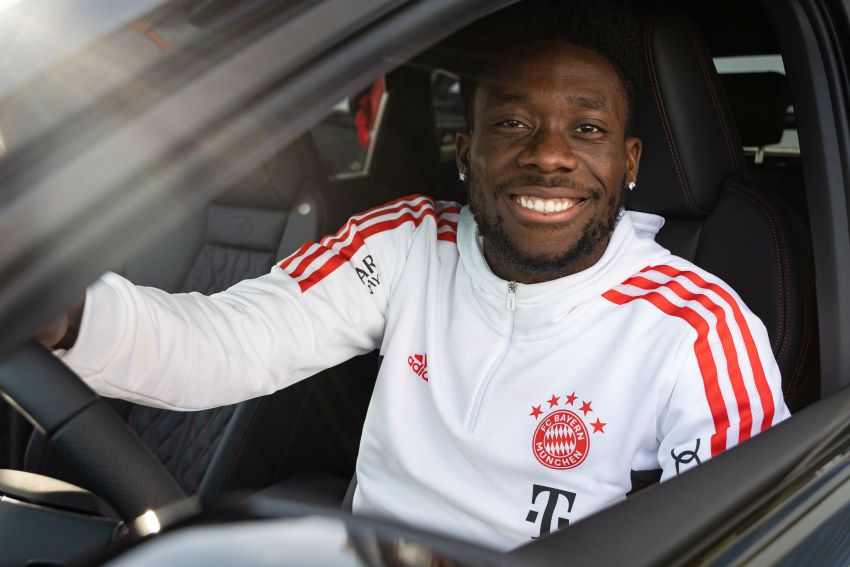 Alphonso Davies dentro de um carro sorrindo para a câmera.