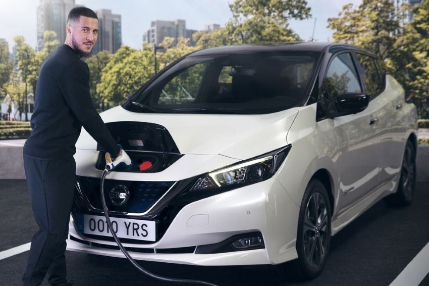 Jogador Eden Hazard, vestido todo de preto, recarrega Nissan Leaf branco