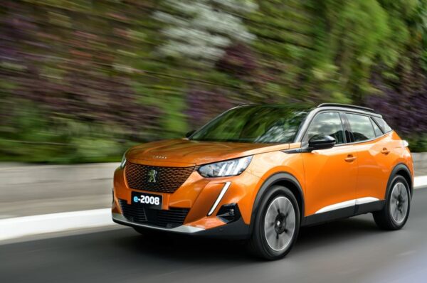 carro Peugeot e-2008 na cor laranja correndo em uma pista com vegetação em volta.