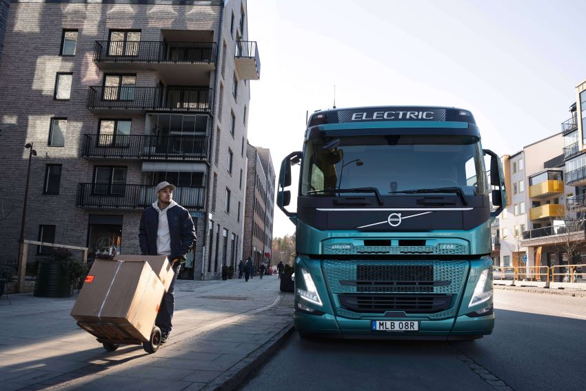 Homem transporta caixa ao lado de caminhão elétrico da Volvo em rua de cidade
