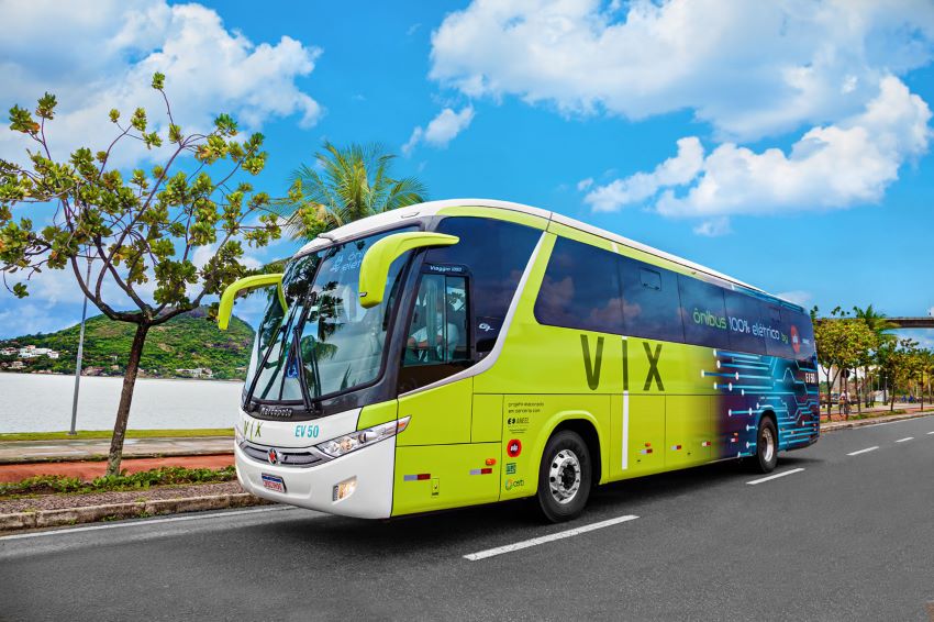 Foto frontal de um onibus na cor verde com na frente e azul na parte de trás, onde se lê "VIX" e mais atrás "ônibus 100% elétrico".