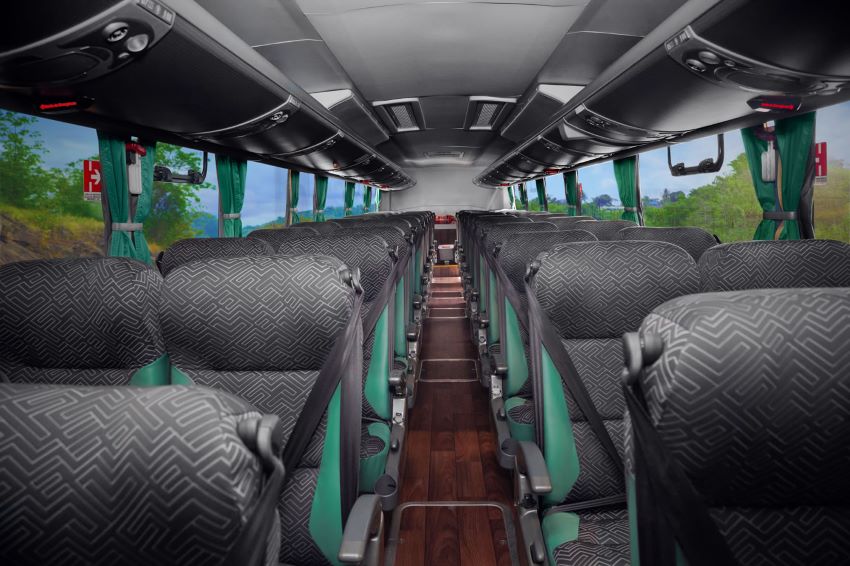 Vários assentos de ônibus enfileirados. O teto do veículo é preto, o chão cor de madeira, e os detalhes dos bancos, também pretos, são verdes.