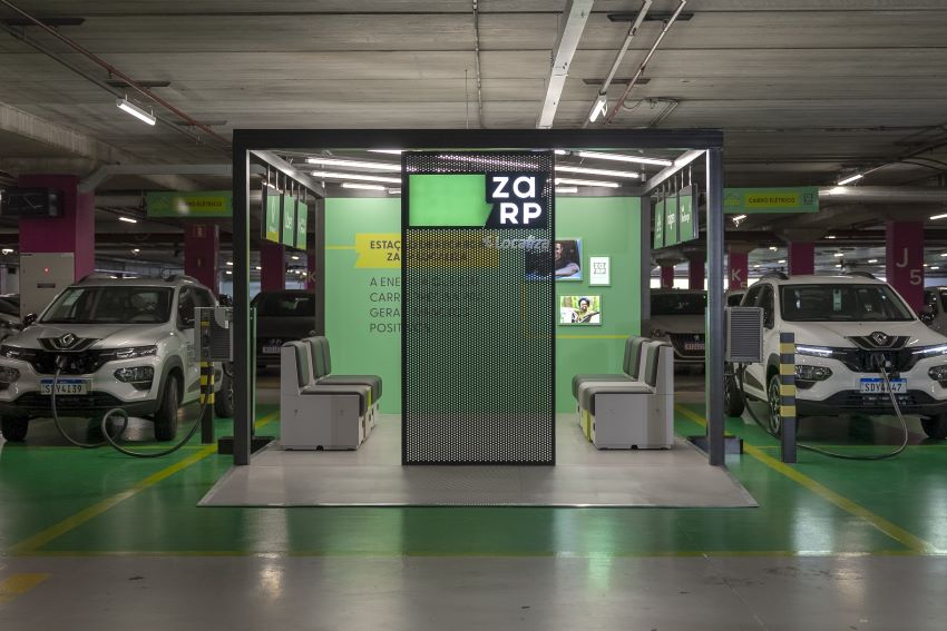 Lounge é um espaço demarcado na cor verde dentro de um estacionamento coberto para o carregamento de carro elétrico, e conta com poltronas em cinza