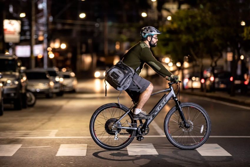 Homem pedala bicicleta elétrica em rua durante à noite