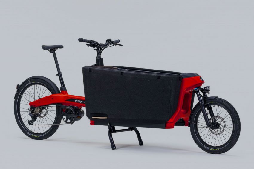 Bicicleta elétrica vermelha tem compatimento de carga preto entre banco do ciclista e roda da frente