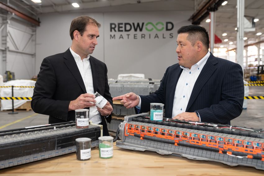Dois homens com roupas de executivos conversam em fábrica da Redwood Materials