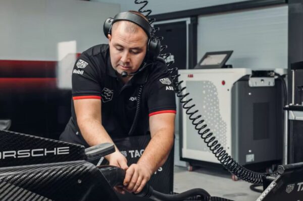 Mecânico da equipe Porsche, usando camiseta preta, conecta carregador no carro pela parte traseira