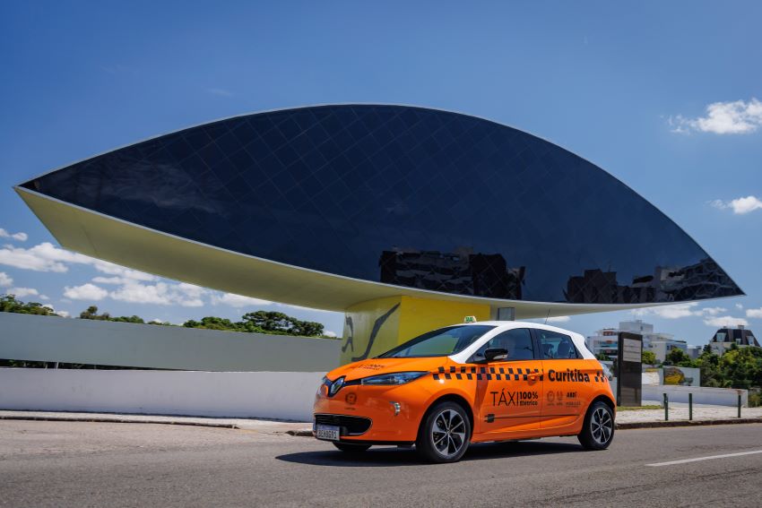 Renault Zoe E-Tech, todo caracterizado como táxi, na cor laranja, circula pelas ruas de Curitiba.