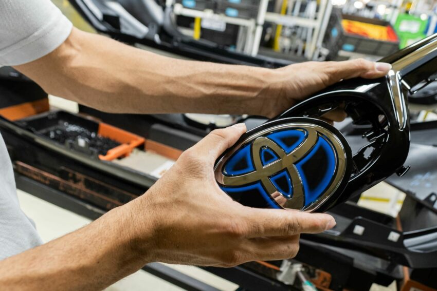 Mãos de funcionário seguram marca da Toyota em fábrica