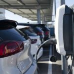 Imagem mostra carros estacionados em frente a um carregador para veículos elétricos