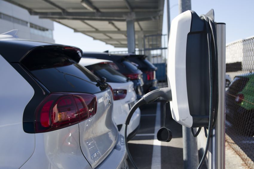 Imagem mostra carros estacionados em frente a um carregador para veículos elétricos