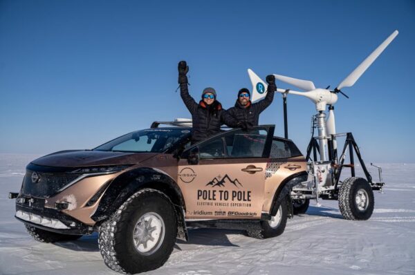 Bem agasalhados, Chris e Julie Ramsey acenam do lado de fora do carro no Polo Norte, com neve ao fundo