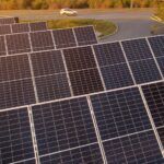 Painéis fotovoltaicos para geração de energia solar estão posicionados ao lado de rodovia, com veículo branco passando ao fundo