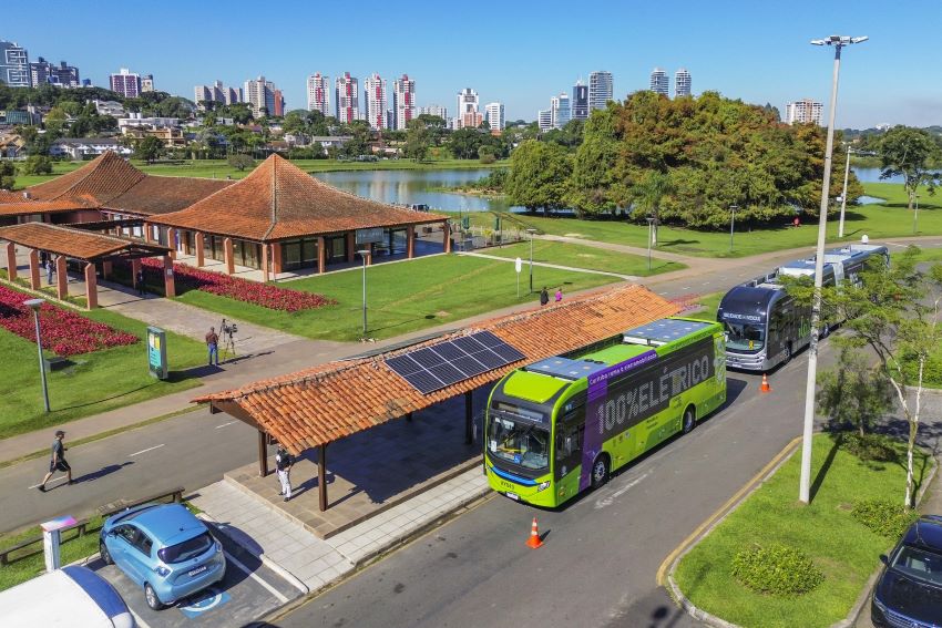 Vista aérea de ônibus elétricos, com a cidade de Curitiba ao fundo
