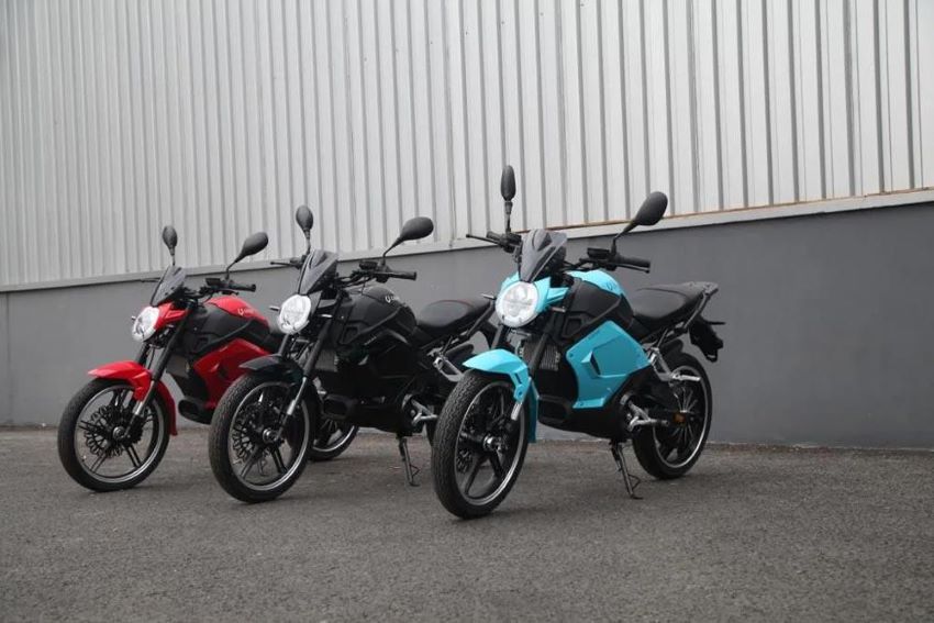 Três motos elétricas estacionadas, uma vermelha, uma preta e uma azul