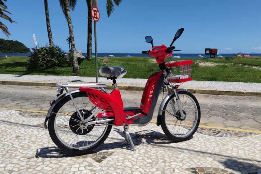 Bicicleta elétrica vermelha estacionada em ciclovia próxima à praia