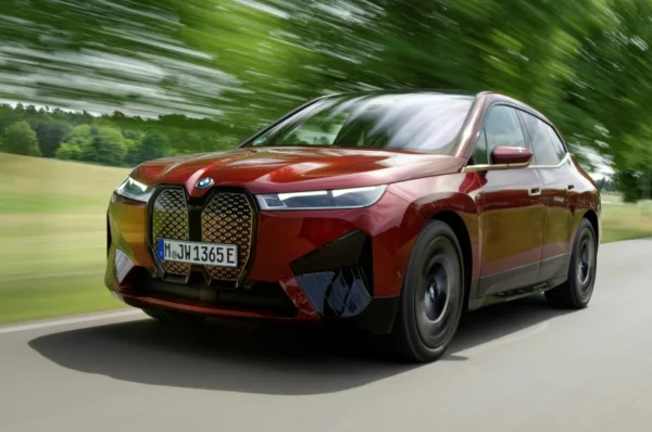 BMW iX M60 vermelho andando em uma estrada com vegetação ao fundo