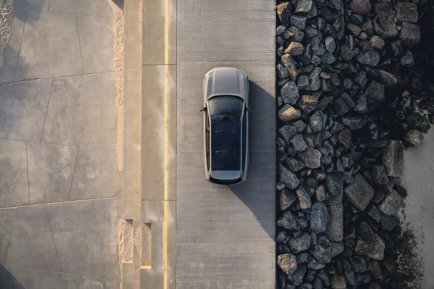 Visão aérea do Volvo EX90 em um cenário de pedras de um lado e areia do outro, próximo ao litoral