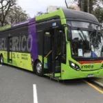 Ônibus elétrico na cor predominantemente verde é visto em rua de Curitiba