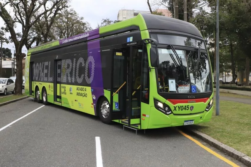 Ônibus elétrico na cor predominantemente verde é visto em rua de Curitiba