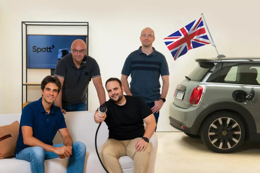 Fundadores da Spott posam para foto em cenário com sofá, carro elétrico e uma bandeira da Grã-Bretanha