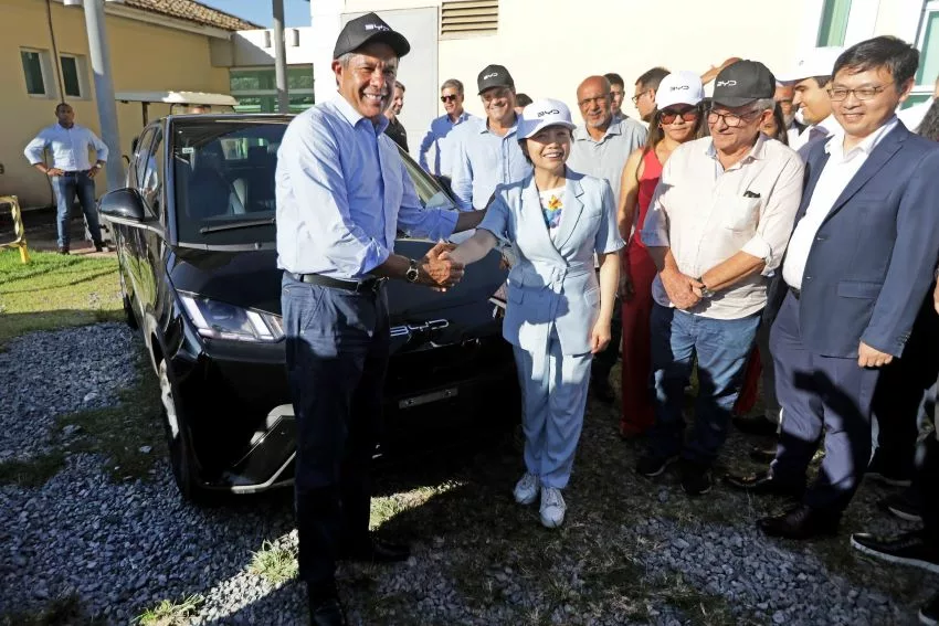 governador da Bahia e vice-presidente global da BYD dão as mãos em frente a carro elétrico da BYD