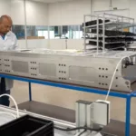 Homem manuseia caixa metálica grande dentro de ambiente de fábrica