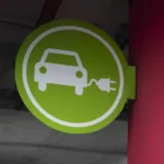 Placa verde com ícone de carro com tomada elétrica afixada em parede vermelha indica estacionamento de veículos elétricos