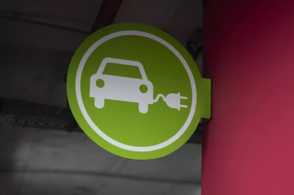 Placa verde com ícone de carro com tomada elétrica afixada em parede vermelha indica estacionamento de veículos elétricos