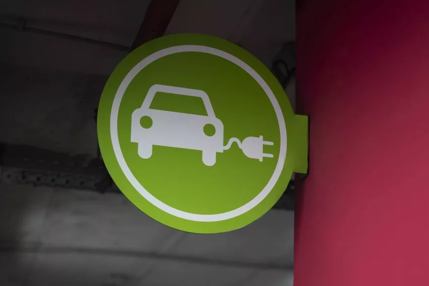 Placa verde com ícone de carro com tomada elétrica afixada em parede vermelha indica estacionamento de veículos elétricos