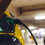 Carro elétrico amarelo recebe recarga em ambiente fechado de estacionamento