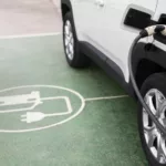 Carro elétrico recebe recarga em estacionamento demarcado com símbolo de carro elétrico