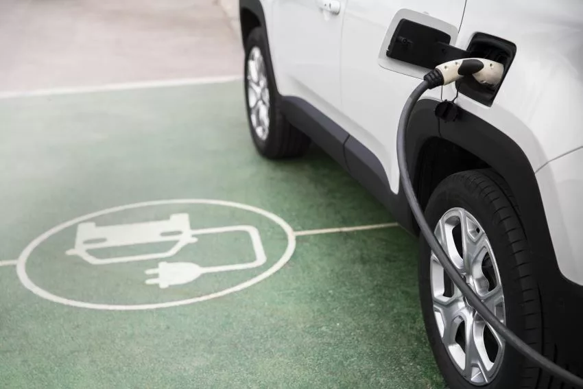 Carro elétrico recebe recarga em estacionamento demarcado com símbolo de carro elétrico
