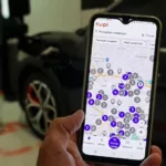 Imagem mostra detalhe do aplicativo Tupi Recarga em smartphone, com carro elétrico desfocado ao fundo
