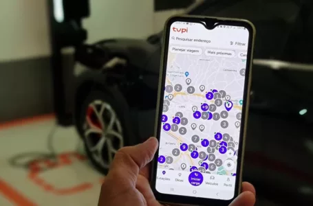 Imagem mostra detalhe do aplicativo Tupi Recarga em smartphone, com carro elétrico desfocado ao fundo