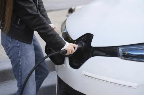 Detalhe de uma mão feminina para a recarga de um carro elétrico