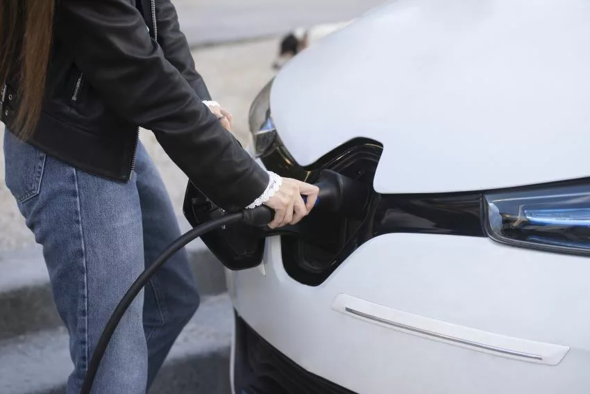 Detalhe de uma mão feminina para a recarga de um carro elétrico