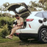 Homem sentado no porta-malas do carro utiliza notebook com energia proveniente do carro