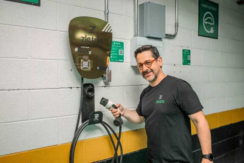 Homem com barba mostra carregador de carro elétrico instalado em parede