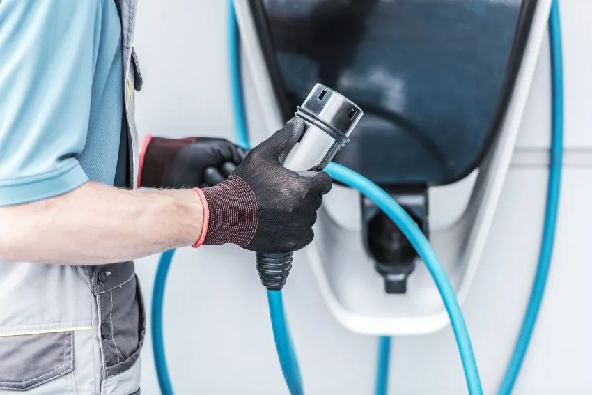 Imagem mostra mãos masculinas manuseando carregador de carro elétrico