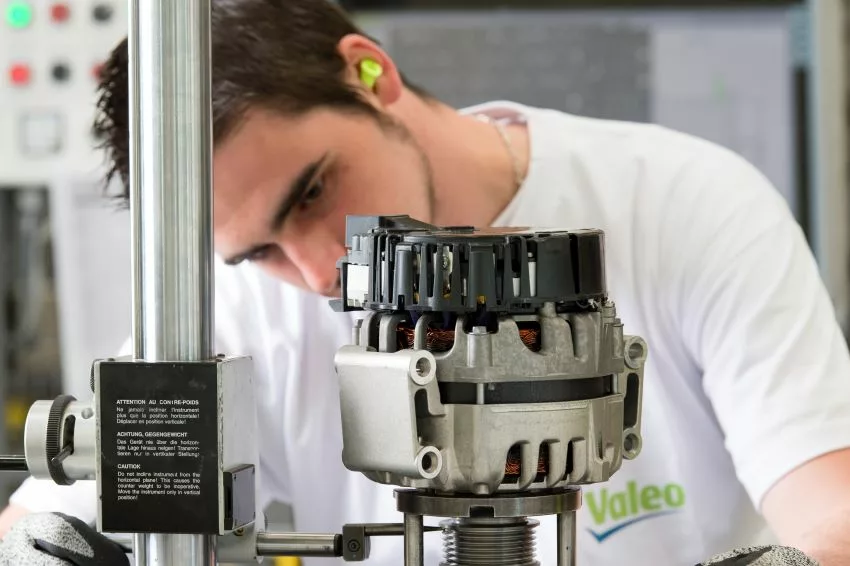 Funcionário com camiseta da Valeo trabalha em peça para carros em linha de montagem