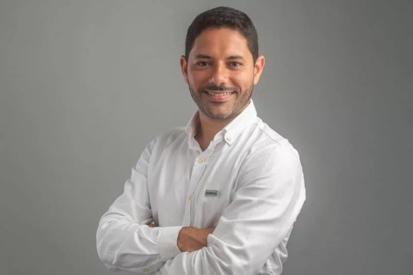 Antonio Neto posa para foto de camisa branca em frente a parede cinza